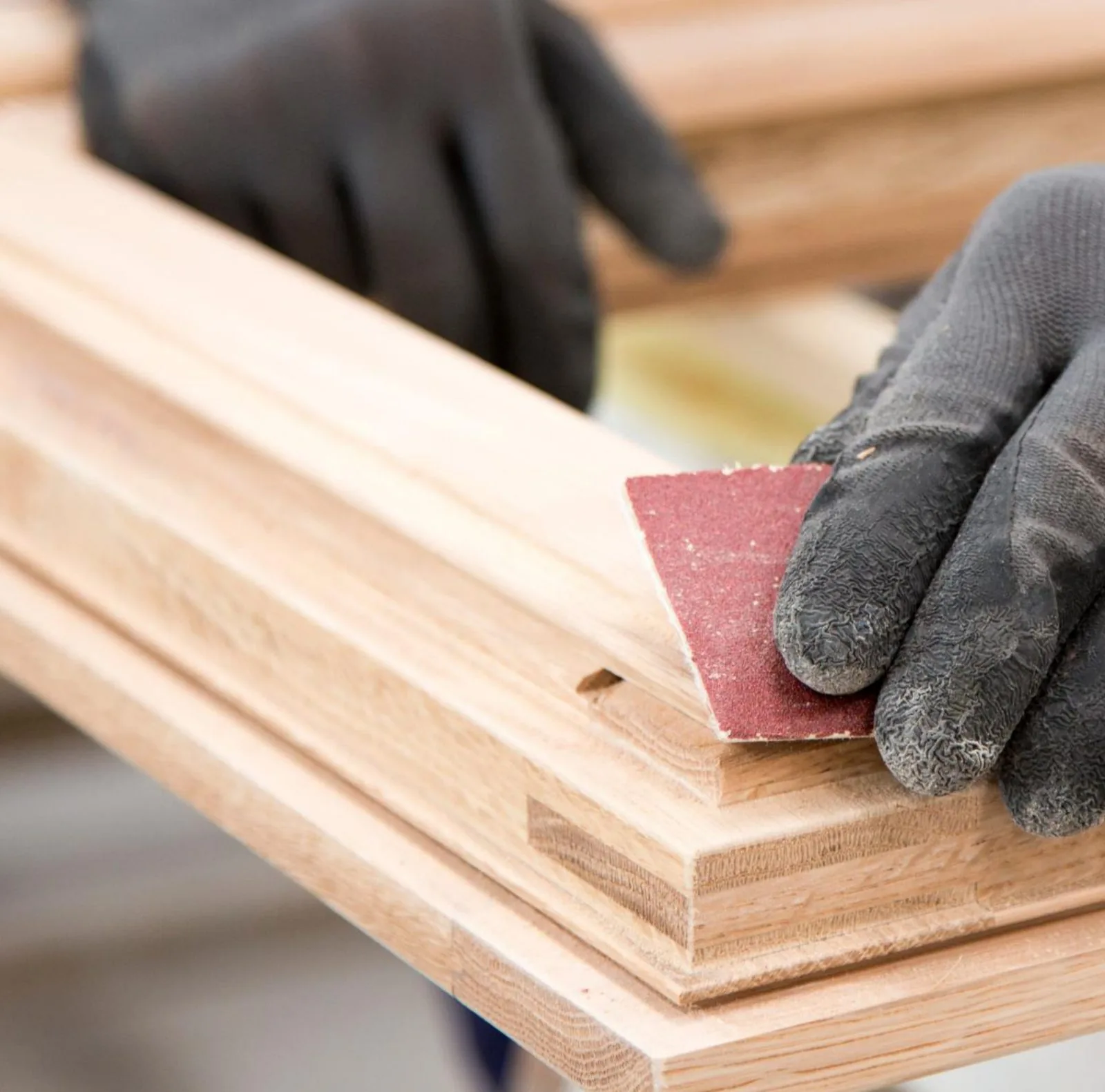 Gloved hands sanding a solid timber window frame by hand in the workshop