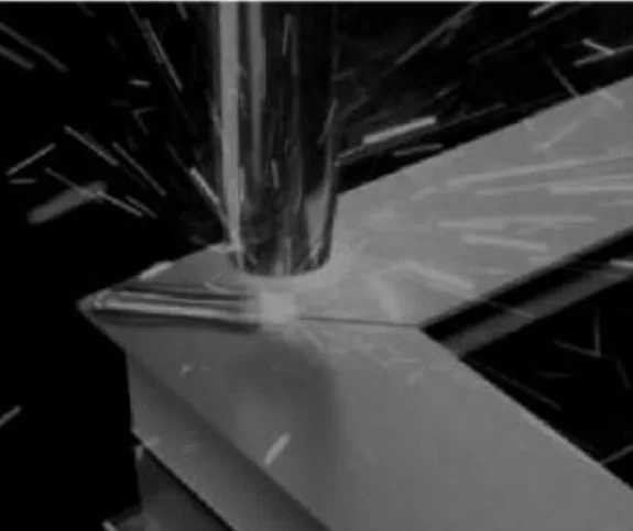 Close-up of an aluminum frame corner being seam-welded, sparks around the weld head