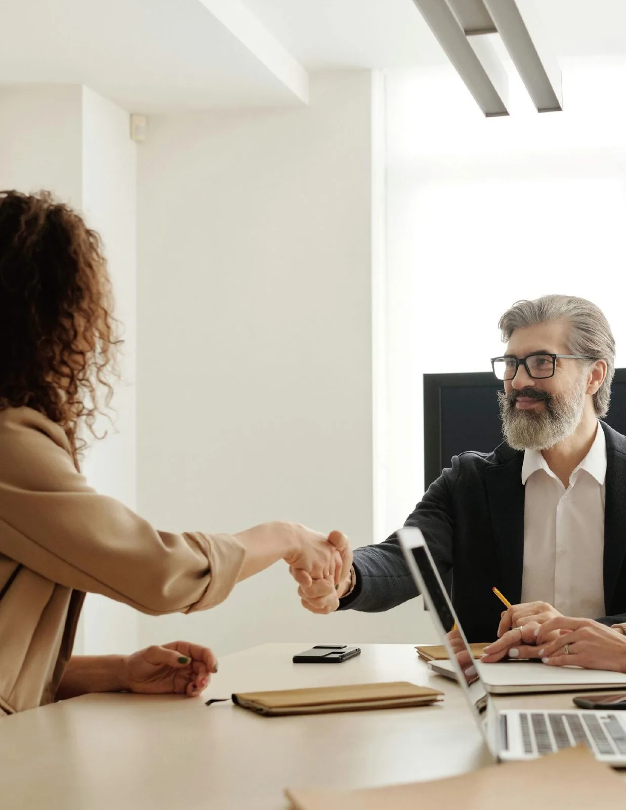 Two people shaking hands across a desk at a project meeting